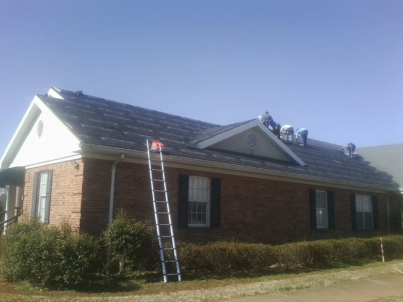 Crew tearing shingles off a brick ranch roof with a ladder set — Emergency Roof Repair work by our crew in Groton